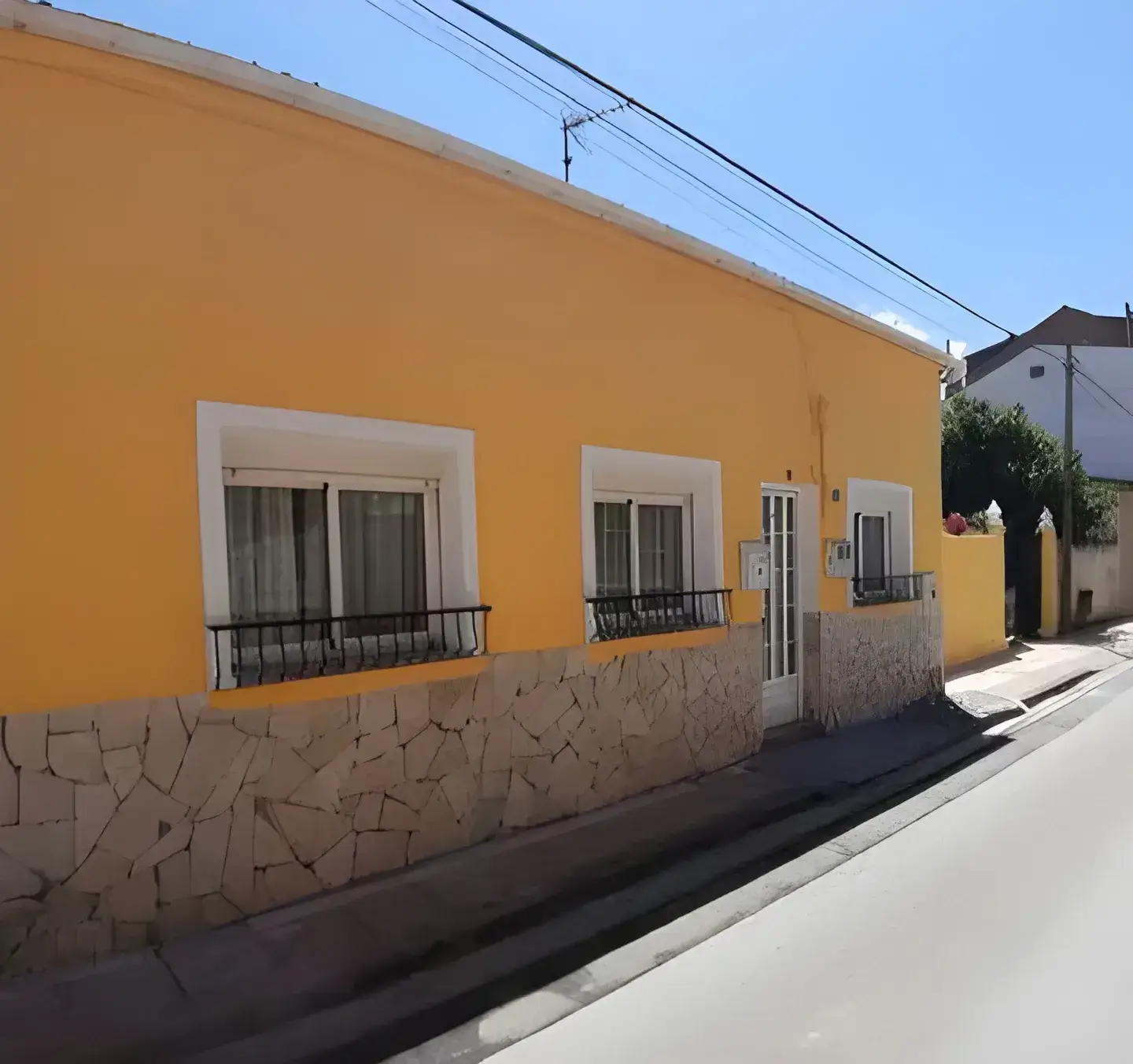 Los Pintores en Córdoba Fachada de casa tradicional pintada en color amarillo con zócalo de piedra